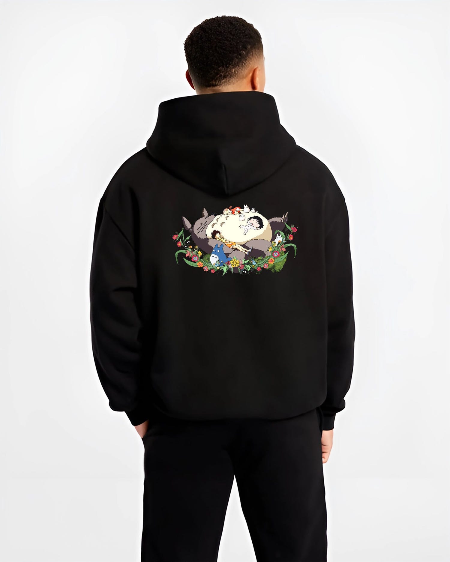 Black hoodie worn by a male model, back view, featuring Totoro sleeping with kids, retro manga graphic and floral nostalgic 90s vibe.