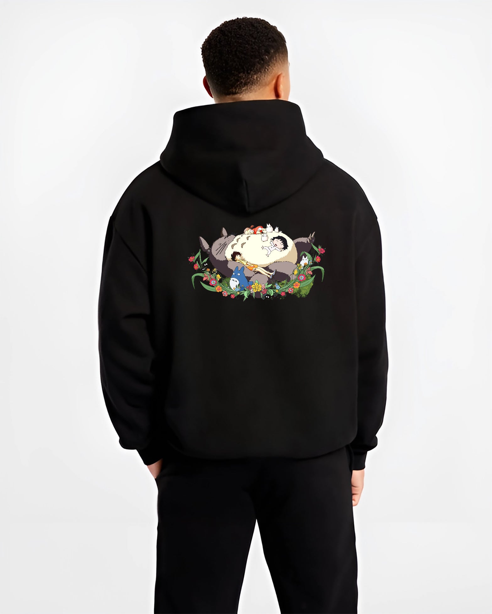 Black hoodie worn by a male model, back view, featuring Totoro sleeping with kids, retro manga graphic and floral nostalgic 90s vibe.