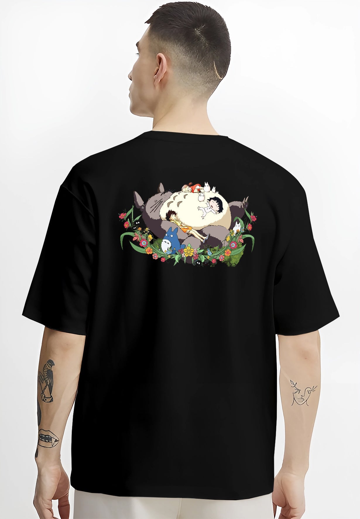Black T-shirt worn by a male model, back view, featuring Totoro sleeping scene, urban fashion back design with nostalgic 90s floral graphic.