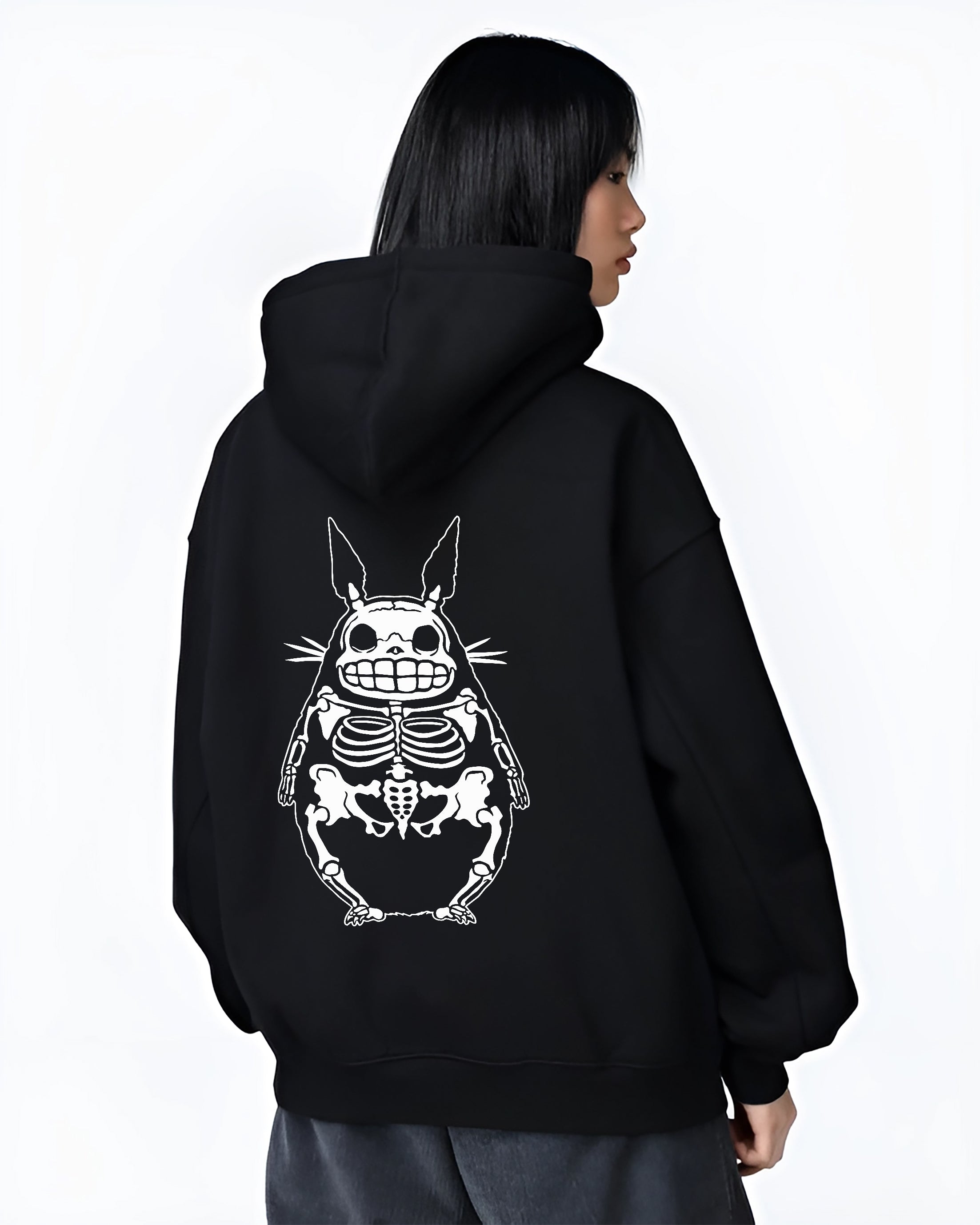 Black hoodie worn by a female model, back view, featuring Totoro skeletal silhouette, Japanese animation streetwear design in bold monochrome line art.