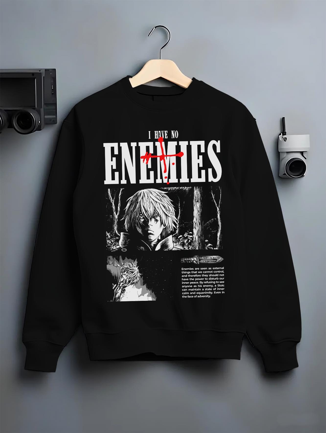 Black crewneck sweatshirt on hanger against grey wall, Vinland Saga Thorfinn panel back graphic with ENEMIES headline.