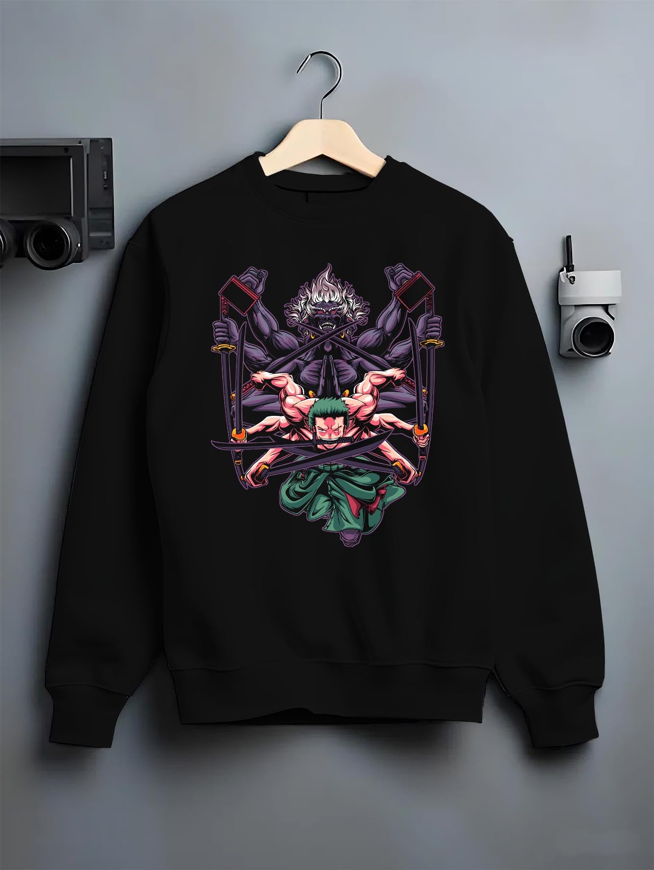 Black crewneck sweatshirt on a hanger against a grey wall, featuring Zoro One Piece retro streetwear graphic with demon aura and manga-inspired three-sword battle art.